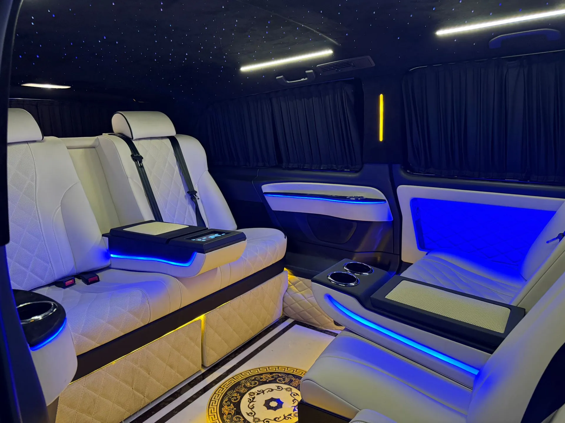 Mercedes V-Class Lounge iç mekan — beyaz deri bank ve döner koltuk, mavi LED ambiyans, tasarım zemin deseni