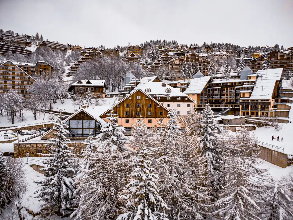 Chalets de station de ski sous la neige, sapins givrés au premier plan